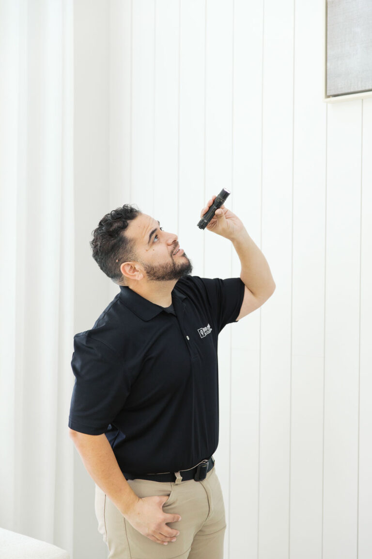 A home inspector using a flashlight to look up at something in the corner of a house.