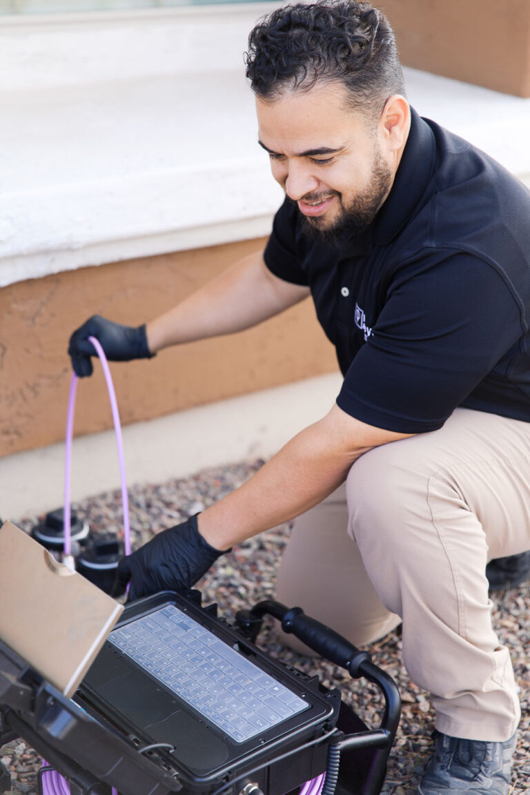 Technician operating sewer inspection camera system outdoors with monitor and push cable during drain inspection.