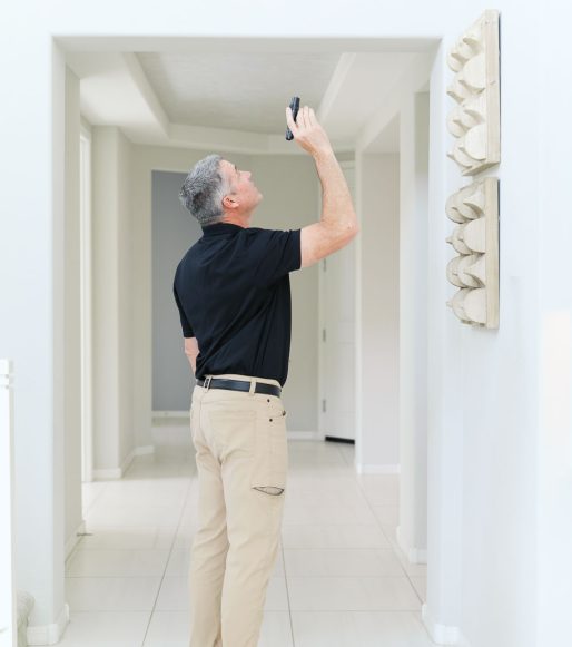A man standing in the hallway of a house, using a flashlight to look up at something.